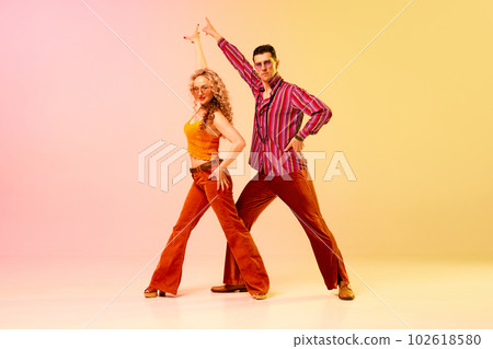 Artistic, expressive man and woman in stylish clothes dancing disco, retro dance against gradient pink yellow background 102618580