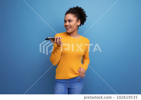 joyful young brunette latin female adult in yellow records voice message 102619535