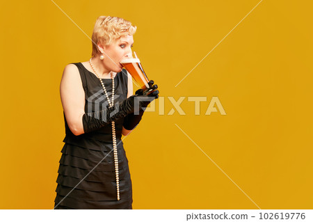 Portrait with lady, woman wearing black vintage dress holding big beer mug and drinking with pleasure over yellow background 102619776