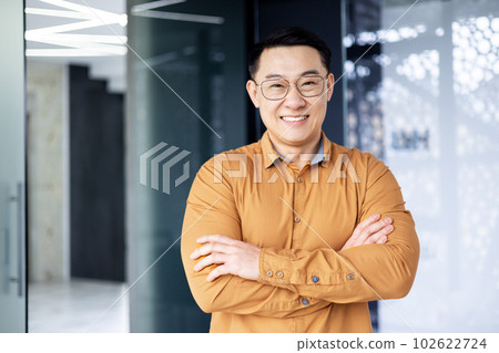 Portrait of successful asian businessman, man inside office wearing shirt and glasses smiling and looking at camera, investor broker with crossed arms near window. 102622724