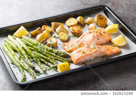 Diet food salmon fillet baked with asparagus and new potatoes close-up in a baking sheet. Horizontal Diet food salmon fillet baked with asparagus and new potatoes close-up in a baking sheet. Horizontal 102623299