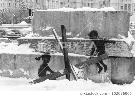 A boy and a girl swing on an anti-tank hedgehog - Banksy graffiti in Kyiv, Ukraine, black and white photo 102626965
