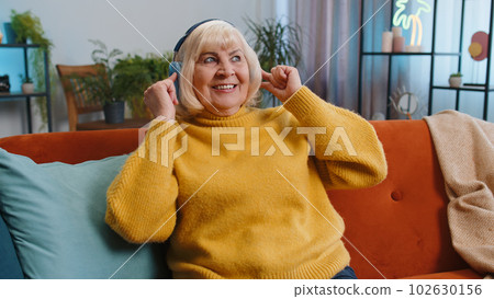 Happy grandmother woman in wireless headphones relaxing on sofa at home listening favorite music 102630156