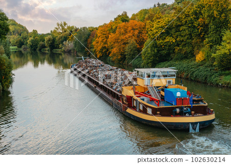 Transportation industry. Ship barge transports scrap metal and sand with gravel. Barge loaded with scrap metal is on the roadstead. Scrap metal transportation by water. Barge laden by metal salvage 102630214