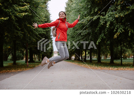 Young caucasian woman girl with toothy smile jumping in park forest outdoors looking at camera. 102630218