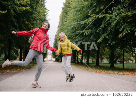 Mother and son jumping in the autumn park. Fall Season. Happy young beautiful mother and her son have a walk in the park 102630222