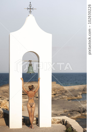 Young sexy woman posing on the beach in Greece. Woman sunbating with mediterranean sea at Santorini island greece. Young woman in a swimsuit on the background of Greek architecture and the sea. Woman 102630226