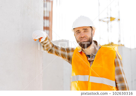 Builder repairman, foreman in safety helmet and vest works at his workplace in a building under construction 102630316