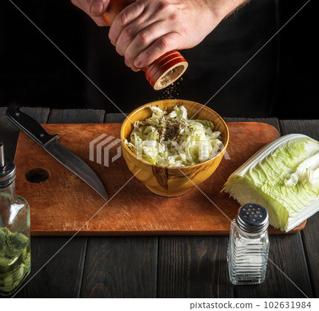 The chef prepares a napa salad. Close up of a chef adding pepper to a salad using a hand mill. Top view 102631984