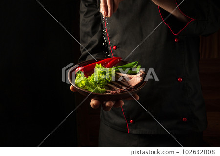Grilled and sliced beef steak with grilled vegetables served on plate on black background presentation in chef hands. 102632008