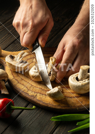 The chef cuts mushrooms Agaricus with knife to prepare delicious food. Set of vegetables on a vintage kitchen table. Delicious recipe for breakfast or lunch 102632009