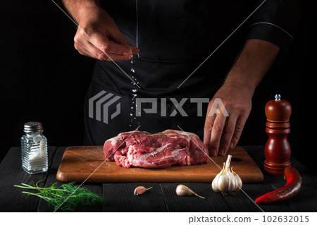 Professional chef sprinkles the meat with salt. Preparing meat before baking. Working environment in the kitchen of restaurant Professional chef sprinkles the meat with salt. Preparing meat before baking. Working environment in the kitchen of restaurant 102632015