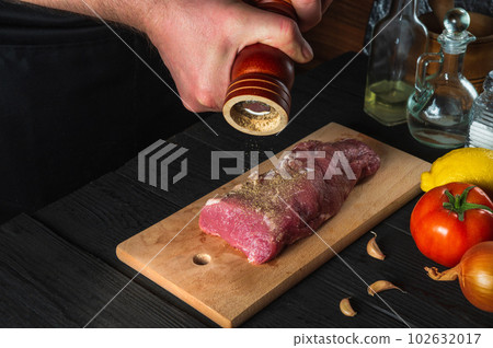 Chef cooking raw meat fillet and adding pepper and chili for marinade on black background. Working environment in kitchen in restaurant or cafe Chef cooking raw meat fillet and adding pepper and chili for marinade on black background. Working environment in kitchen in restaurant or cafe 102632017