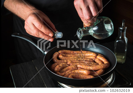 The chef adds oil to pan with raw meat sausage. Preparation for cooking sausages in kitchen of a restaurant or cafe on table with vegetables The chef adds oil to pan with raw meat sausage. Preparation for cooking sausages in kitchen of a restaurant or cafe on table with vegetables 102632019