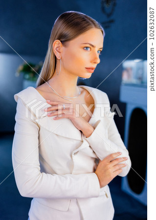 Adoarable beautiful model stands in mirror in a jewelry store tries on a gold diamond necklace that sparkles on the girl. Girl is adorned with golden jewelry and diamonds in a luxurious boutique. Adoarable beautiful model stands in mirror in a jewelry store tries on a gold diamond necklace that sparkles on the girl. Girl is adorned with golden jewelry and diamonds in a luxurious boutique. 102632087
