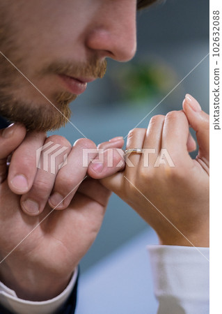 Man in a suit holding hand his bride in a jewelry store, tenderly kissing. Girl tries on a gold diamond high heel in a luxurious and expensive boutique. The loving couple is in a store with gold. Man in a suit holding hand his bride in a jewelry store, tenderly kissing. Girl tries on a gold diamond high heel in a luxurious and expensive boutique. The loving couple is in a store with gold. 102632088