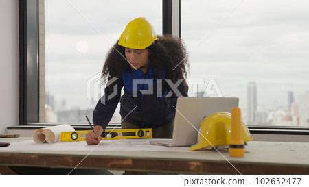 Hardworking female architect with yellow helmet drawing on blueprint 102632477