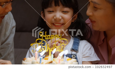 Happy girl surrounded by family making wish and blowing out candles on cake Happy girl surrounded by family making wish and blowing out candles on cake 102632497