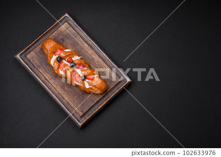 Delicious fresh crispy pastry in the form of a pigtail with strawberries and blueberries Delicious fresh crispy pastry in the form of a pigtail with strawberries and blueberries 102633976