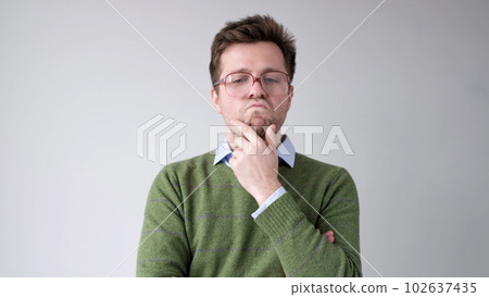 A European young man is rubbing his chin in doubt, thinking and making plans. A European young man is rubbing his chin in doubt, thinking and making plans. 102637435