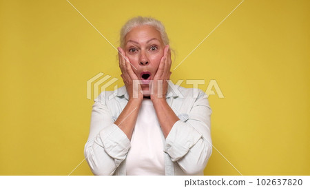 An elderly European woman is inspired, screaming wow and raising her hands in the air. 102637820