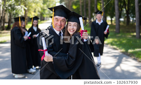 A group of graduates in robes outdoors. An elderly man and a young woman congratulate each other on their graduation. A group of graduates in robes outdoors. An elderly man and a young woman congratulate each other on their graduation. 102637930