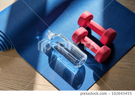 Reusable glass water bottle on a yoga mat with dumbbells. 102643455