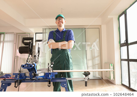Builder with crossed arms stands by disk saw machine in room Builder with crossed arms stands by disk saw machine in room 102648464