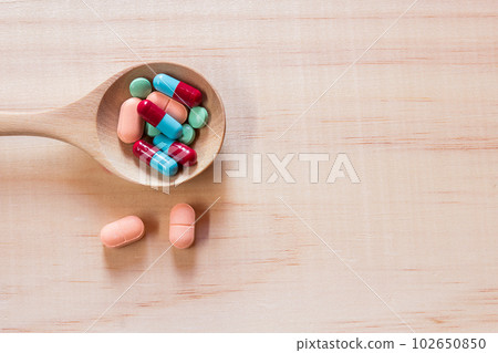 Close up pills in wood spoon on wooden table background. 102650850