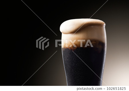 Dark beer, cold beer with bubbles overflowing from glass with water droplets 102651825