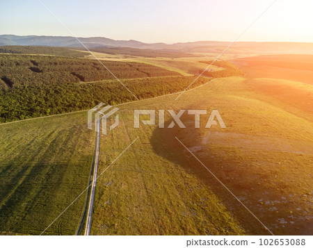 Aerial view on green wheat field, road and hills in countryside. Field of wheat blowing in the wind on sunset. Ears of barley crop in nature. Agronomy, industry and food production. 102653088