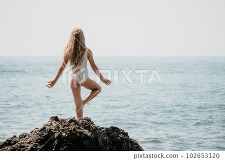 Woman and her daughter practicing balancing yoga pose on one leg up together on rock in the sea. Silhouette mother and daughter doing yoga at beach 102653120