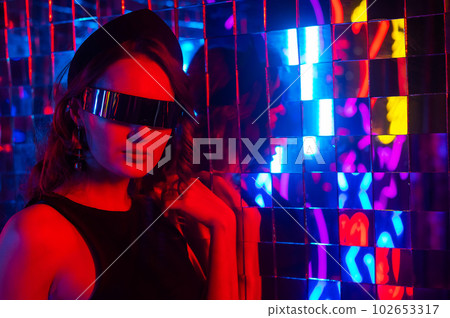 Close-up portrait of a caucasian woman in sunglasses in neon light against a mirror wall. Close-up portrait of a caucasian woman in sunglasses in neon light against a mirror wall. 102653317