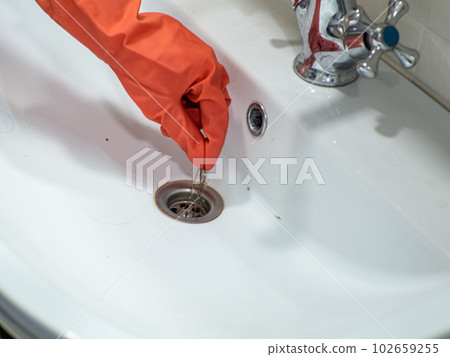 Hand in orange gloves holds many hair loss on filter in washbasin while cleaning 102659255