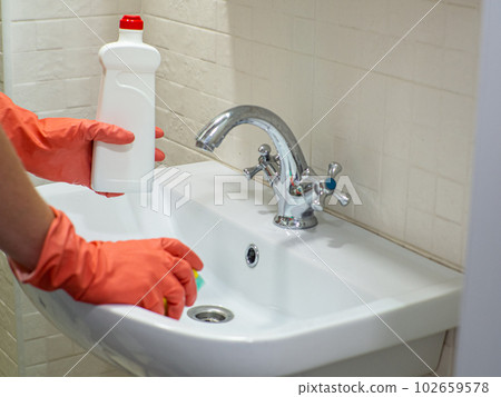 Person hand holding a detergent in white bottle for cleaning bathroom sink Person hand holding a detergent in white bottle for cleaning bathroom sink 102659578