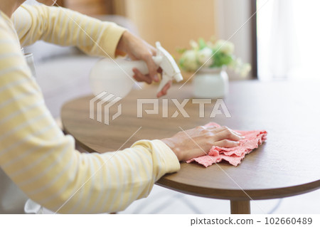 Maid spraying cleaner on wood table and wiping dirty with microfiber fabric to cleaning in home 102660489