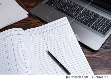 Accounting journal and laptop. Hand on book for accounting. Keep bookkeeping. 102660913