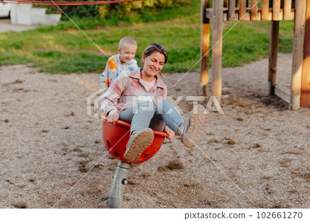 Mother and son having fun on a swing. Motherhood and childhood concept. Sunny summer day. Beautiful family is having fun outside. Parents with children riding on a swing. Mom is playing with her Mother and son having fun on a swing. Motherhood and childhood concept. Sunny summer day. Beautiful family is having fun outside. Parents with children riding on a swing. Mom is playing with her 102661270