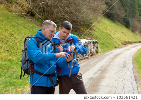 Two hikers are in the mountains in the spring nature outdoor. Hiking with backpacks. Two friends travel together in picturesque places. The man shows the way. Two men on a hiking trip in the mountains 102661421