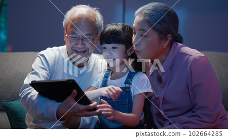 Granddaughter using tablet with senior grandfather and grandmother at home 102664285