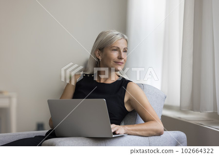 Thoughtful positive blonde mature woman resting in armchair Thoughtful positive blonde mature woman resting in armchair 102664322