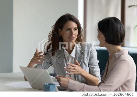 Two attractive businesswomen sit at desk discuss project details Two attractive businesswomen sit at desk discuss project details 102664605