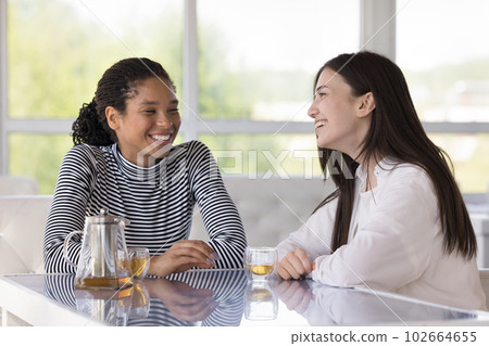 Two pretty millennial women talking seated at table in cafe 102664655
