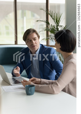 Two serious middle-aged business people negotiate in office Two serious middle-aged business people negotiate in office 102664663