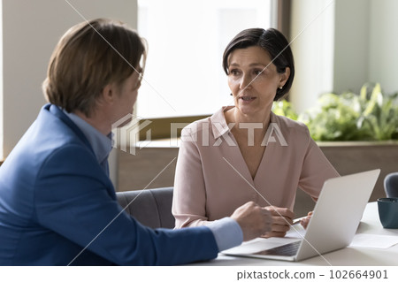 Two business people talking sit at desk with laptop Two business people talking sit at desk with laptop 102664901