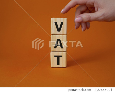 VAT - Value Added Tax symbol. Wooden cubes with word VAT. Businessman hand. Beautiful orange background. Business and Value Added Tax concept. Copy space. VAT - Value Added Tax symbol. Wooden cubes with word VAT. Businessman hand. Beautiful orange background. Business and Value Added Tax concept. Copy space. 102665991