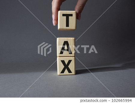 Tax symbol. Wooden cubes with word Tax. Businessman hand. Beautiful grey background. Business and Finace and Tax concept. Copy space. Tax symbol. Wooden cubes with word Tax. Businessman hand. Beautiful grey background. Business and Finace and Tax concept. Copy space. 102665994
