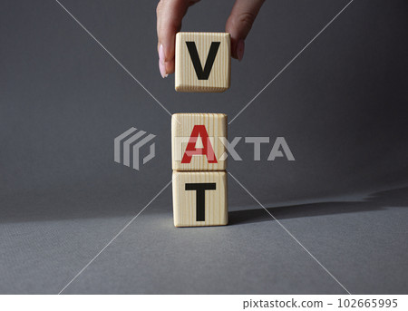 VAT - Value Added Tax symbol. Wooden cubes with word VAT. Businessman hand. Beautiful grey background. Business and Value Added Tax concept. Copy space. 102665995