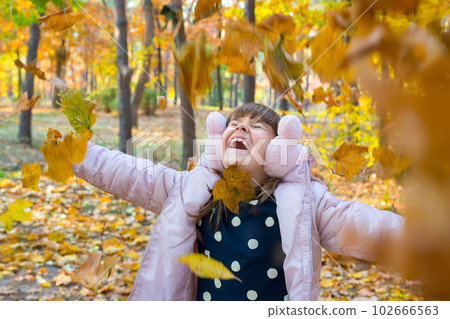 Happy little girl plays in a sunny autumn park with yellow autumn leaves. Life style, Golden hour Happy little girl plays in a sunny autumn park with yellow autumn leaves. Life style, Golden hour 102666563