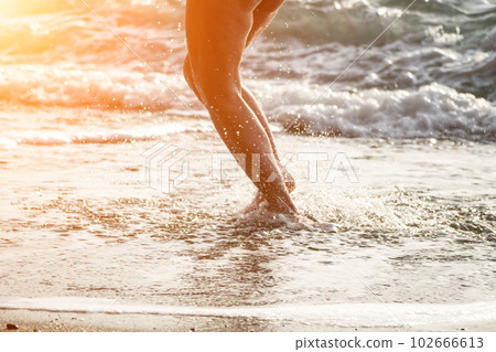 Running woman on a summer beach. A woman jogging on the beach at sunrise, with the soft light of the morning sun illuminating the sand and sea, evoking a sense of renewal, energy and health. 102666613